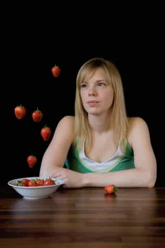 Young woman sitting at table looking at strawberries floating mid-air Stock Photos
