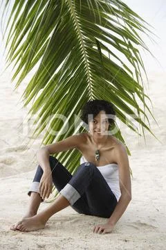 Young woman sitting under palm tree and smiling. Stock Photos