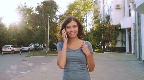 Young woman with smartphone walking in the city with sun, steadicam shot Stock Footage