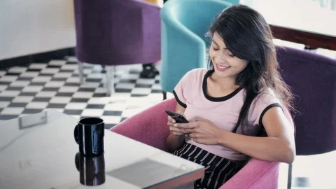 Young woman smiles while using cellphone in a modern cafe Stock Footage 97313097