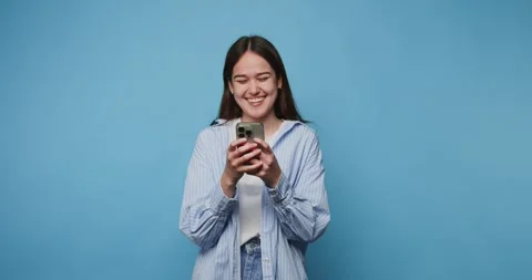 Young woman smiles while using smartphone against a blue background in a ca.. Stock Footage 313273821