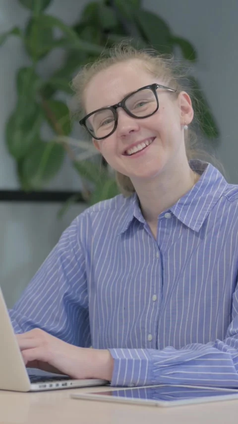 Young Woman Smiling at Camera while Working on Laptop, vertical video 스톡 동영상 328549392