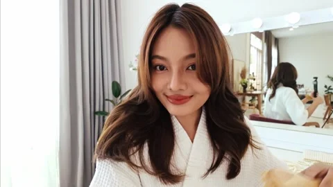 Young woman smiling while brushing her hair in front of a mirror at home. 動画素材 310542855
