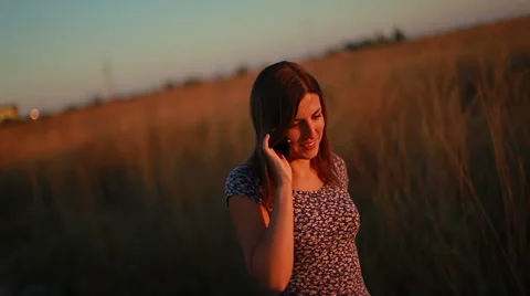 Young woman smiling while cell phone talk walking on a field at sunset Stock Footage 68821013