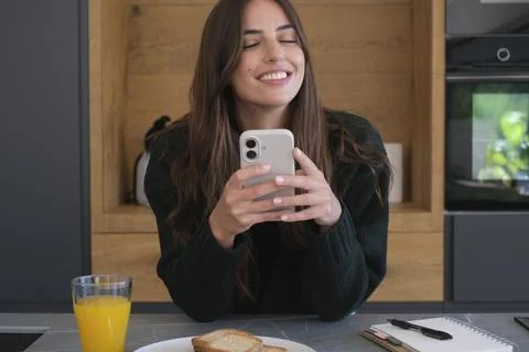 Young woman smiling while checking her smartphone during a relaxed breakfas.. Stock Photos