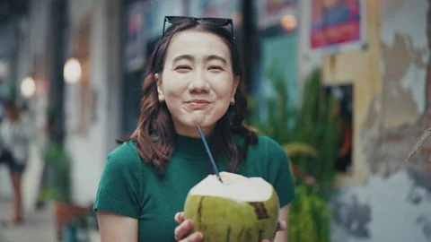 Young woman smiling while holding a fresh coconut drink outdoors Stock Footage 319762395