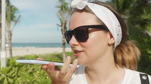 Young woman smiling while recording a voice message on a smartphone, enjoying a Stock Footage 320056906