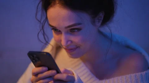 Young woman smiling while texting on smartphone at night Stock Footage 333562749