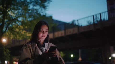 Young woman smiling while typing into her phone at night Stock Footage 203587914