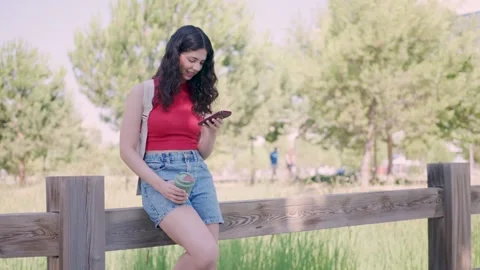 Young woman smiling while using smartphone in a park Stock Footage 339007303