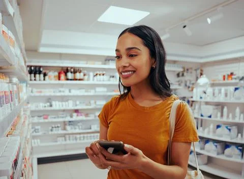 Young woman smiling while using smartphone to read prescription and chose Stock Photos