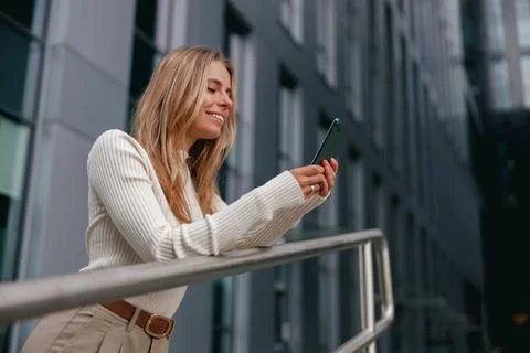 A Young Woman is Smiling While Using Her Smartphone in a Vibrant Urban Stock Photos