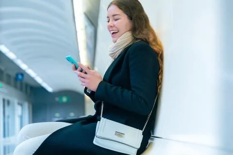 Young Woman Smiling While Using Smartphone in Modern Subway Station Stock Photos