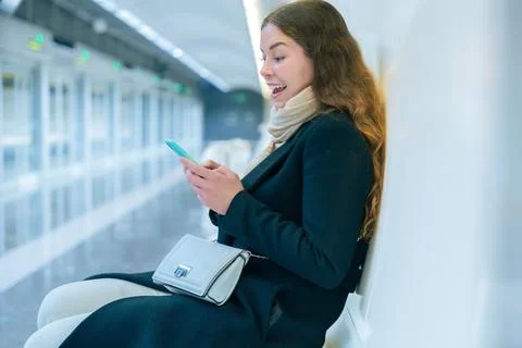 Young Woman Smiling While Using Smartphone in Modern Subway Station Stock Photos
