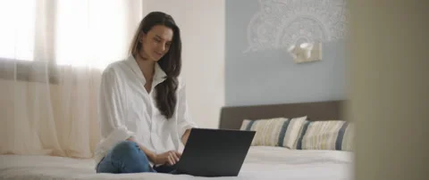 A young woman smiling while working on a laptop from her bedroom. Stock Footage 132366413