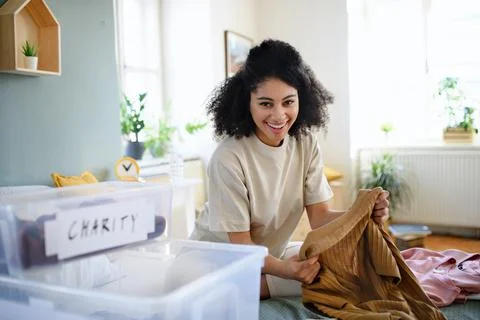 Young woman sorting wardrobe indoors at home, charity donation concept. Stock Photos