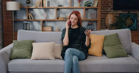 Young woman speaking using mobile phone, sitting on sofa in living room. Famale Stock Footage 225468051