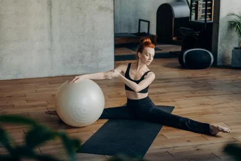 Young woman in split position exercising with fitball in fitness studio Stock Photos