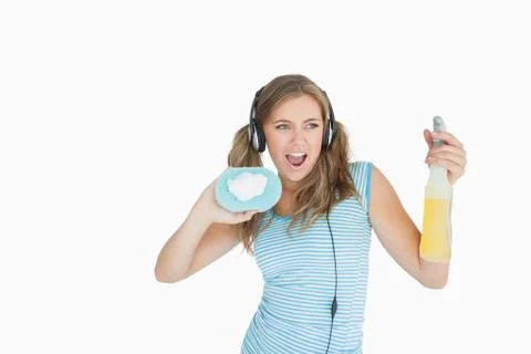 Young woman with sponge and spray bottle enjoying music over headphones Stock Photos