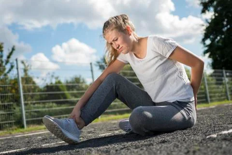 A young woman in sportswear is sitting on the sports field and looks painful Stock Photos