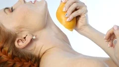 Young Woman Squeezing Orange on Neck and a Breast on a White