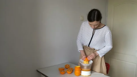 Young woman is squeezing oranges using electric juicer in the kitchen. Stock Footage 158529308