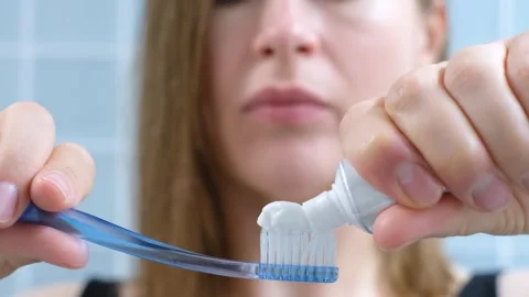 Young woman squeezing toothpaste on a toothbrush on blue background, selective Stock Footage 252330893