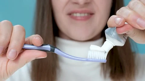 Young woman squeezing toothpaste on toothbrush on blue background. Stock Footage 302327800
