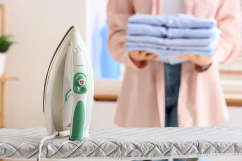 Young woman with stack of clothes and iron on board at home, closeup Stock Photos