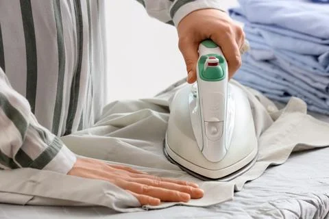 Young woman with stack of clothes ironing shirt on board at home, closeup Stock Photos