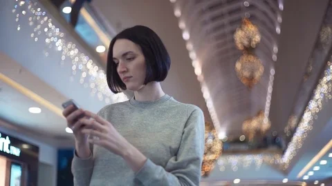 Young woman standing alone using smartphone in shopping mall Stock Footage 83366970