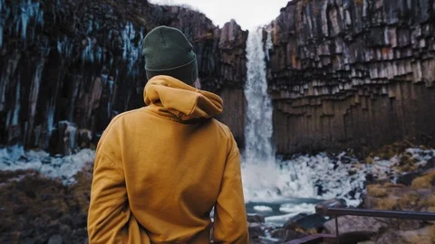 A young woman standing and looking at the bottom of a waterfall in Iceland. Stock Footage