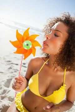 Young woman standing in beachwear while blowing on a pinwheel Stock Photos