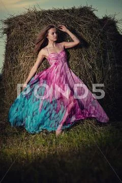 Young woman standing in evening field over haystack. Fashion sty Stock Photos