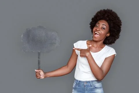 Young woman standing isolated on gray pointing at cloud looking camera excited Stock Photos