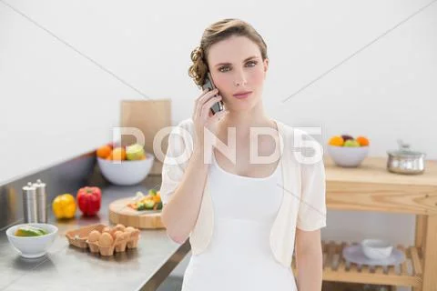 Young woman standing in kitchen while phoning Stock Photos