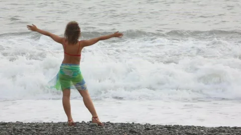 Young woman standing on pebble beach against waves of sea Stock Footage