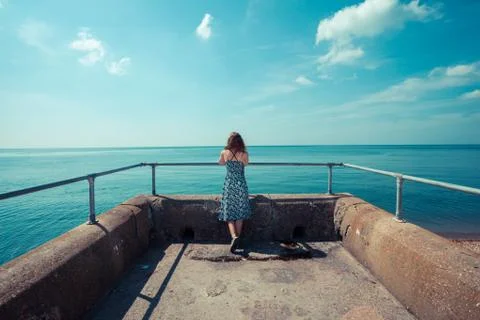 Young woman standing on a pier by the ocean Stock Photos