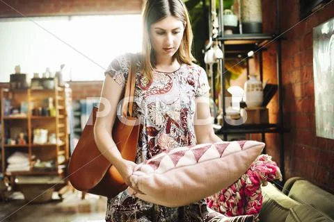 Young woman standing in a shop, holding a cushion. Stock Photos
