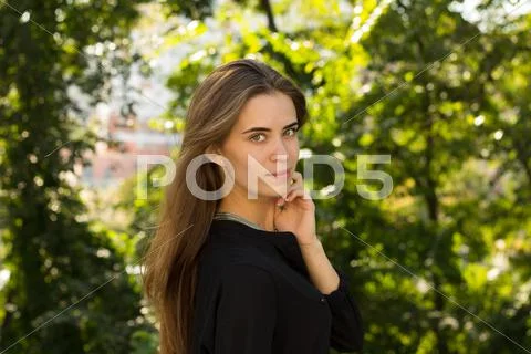 Young woman standing sidewise on the background of trees Stock Photos