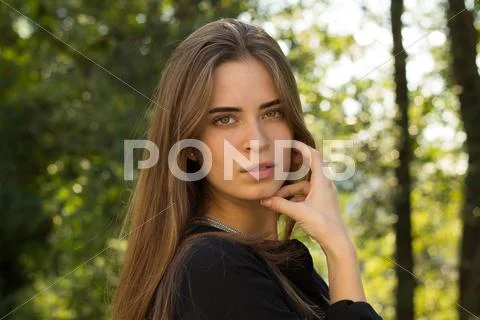Young woman standing sidewise on the background of trees Stock Photos
