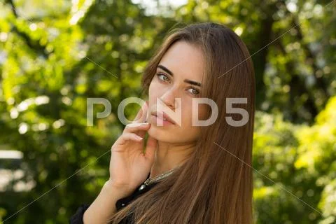 Young woman standing sidwise on the background of trees Stock Photos