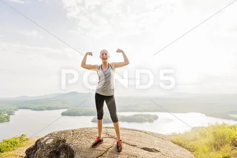 Young woman standing on top of mountain and flexing muscles Stock Photos