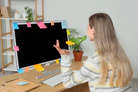 Young woman with sticky notes on computer monitor working in office, back vie Stock Photos