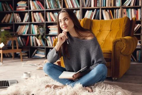 Young woman student in library at home sitting looking up dreaming Stock Photos