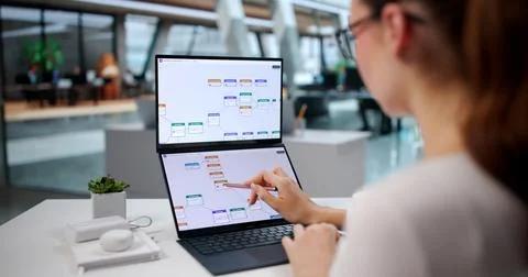Young Woman Studies Workflow Data On Dual Touchscreen Laptop At Office. 写真素材
