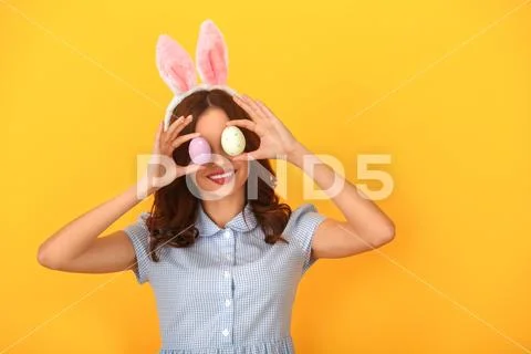 Young woman studio isolated on yellow wearing bunny ears covering eyes with eggs Stock Photos