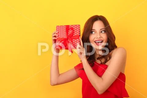 Young woman studio isolated on yellow in a red dress shaking present box Stock Photos