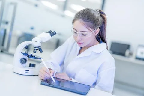 Young woman studying with a tablet while using a microscope in a science la.. Stock Photos