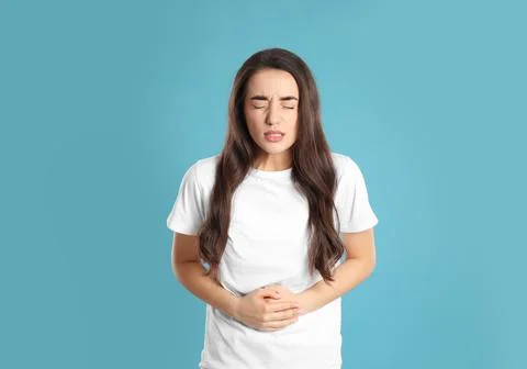 Young woman suffering from stomach ache on light blue background. Food poison Stock Photos